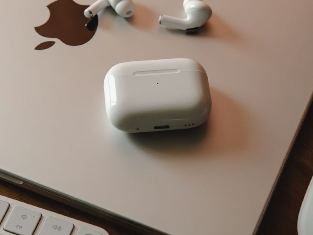 MacBook with wireless earphones and keyboard on a wooden desk, a tech-savvy workspace.