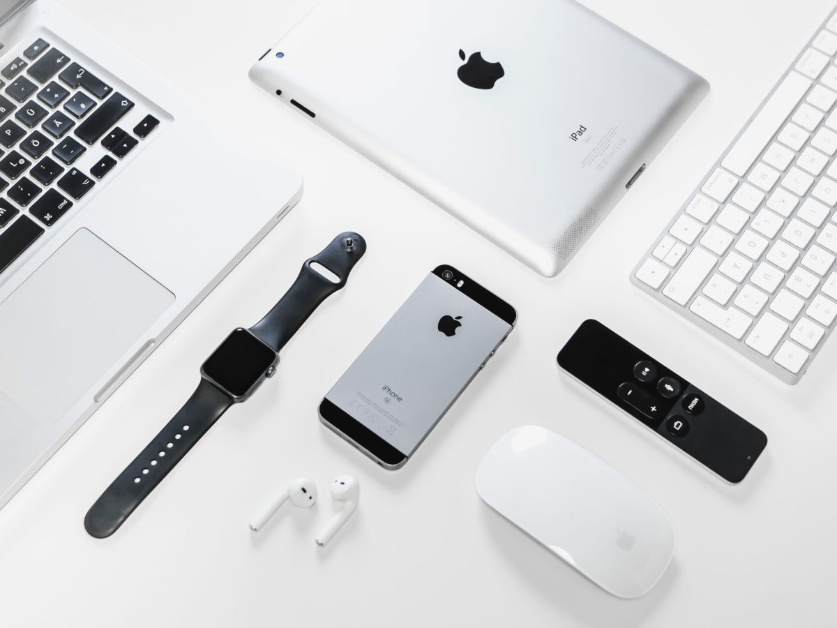 Flat lay of Apple devices including iPhone, iPad, MacBook, and Watch on a white surface, ideal for tech enthusiasts.